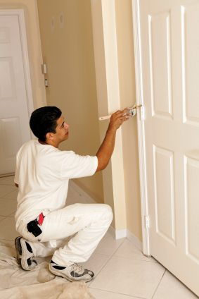 Painter painting interior of house. Painting the trim around a door white.
